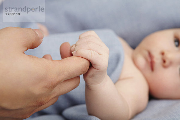 Baby Junge hält Mütter Finger im Bett