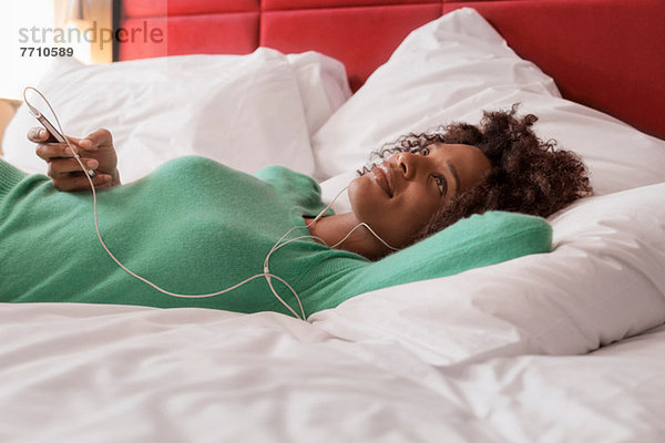 Frau hört Kopfhörer auf dem Bett
