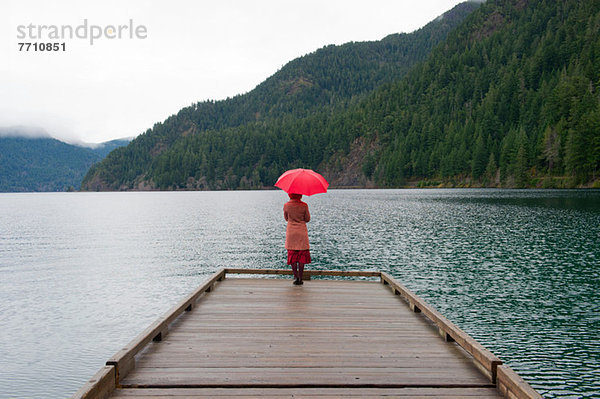Frau mit Regenschirm auf Holzpfeiler