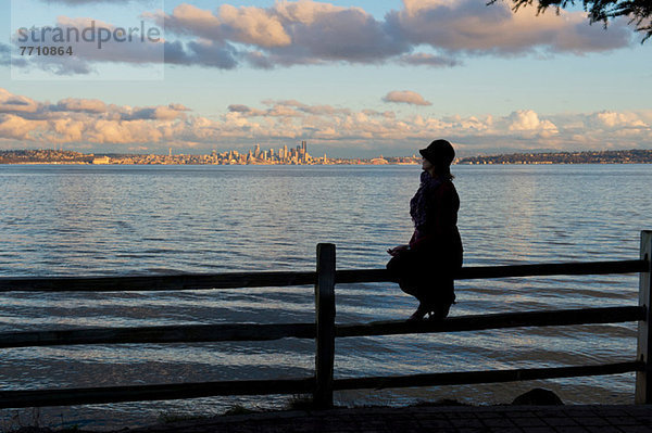 Silhouette der Frau auf dem Zaun sitzend