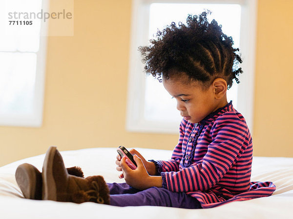 Mädchen spielt mit Handy im Bett