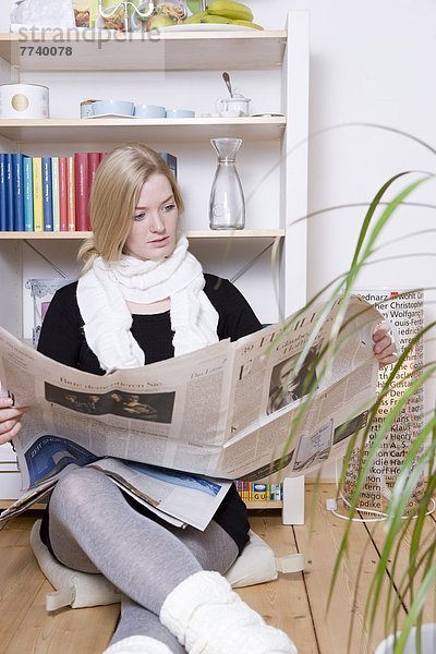 Blonde Frau sitzt Zeitung lesend auf dem Boden