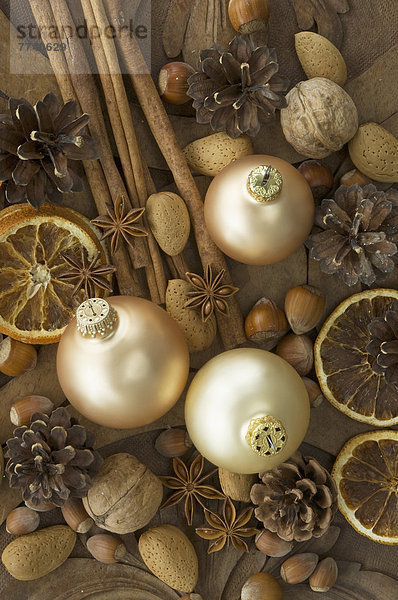 Weihnachtskugeln mit getrockneten Orangenscheiben  Zimtstangen  Walnüssen  Haselnüssen  Mandeln und Tannenzapfen auf Tisch