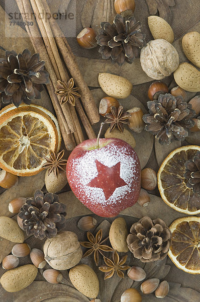 Weihnachtsapfel mit Schneestern  Haselnüssen  Walnüssen  Mandeln  Sternanis  Zimtstangen  getrockneten Orangenscheiben und Pinienzapfen auf dem Tisch