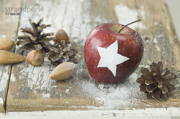 Weihnachtsapfel mit Schneestern  Pinienzapfen  Mandeln und Haselnüssen auf dem Tisch