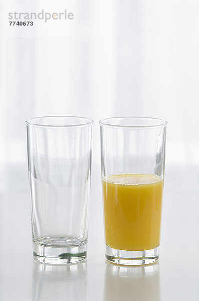 Glas Orangensaft neben leerem Glas auf weißem Hintergrund  Nahaufnahme