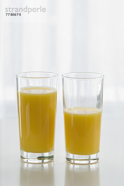 Orangensaftgläser auf Tisch vor weißem Hintergrund  Nahaufnahme