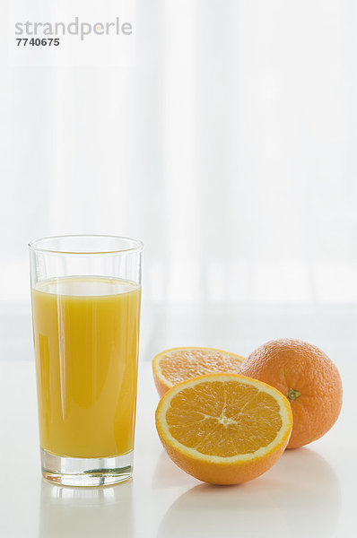 Glas Orangensaft mit Orangen auf Tisch vor weißem Hintergrund  Nahaufnahme