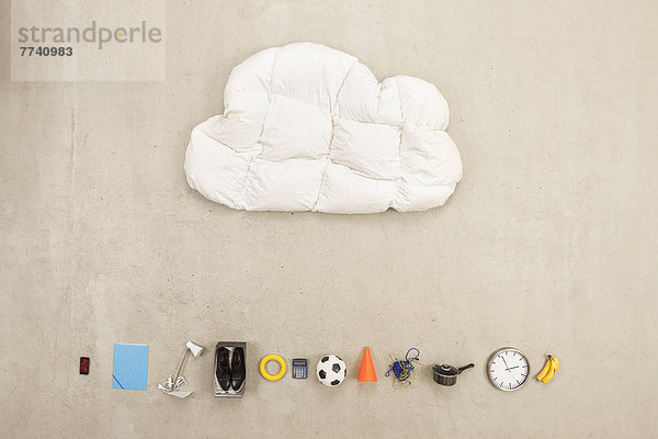 Wolkenförmiges Kissen mit verschiedenen Artikeln auf beigefarbenem Hintergrund