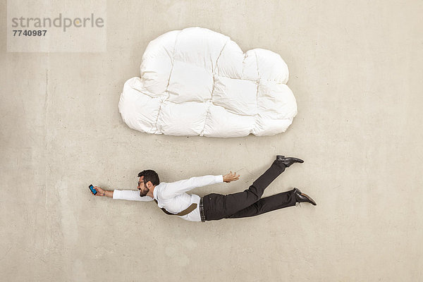 Geschäftsmann hält Handy und fliegt unter Wolkenform Kissen