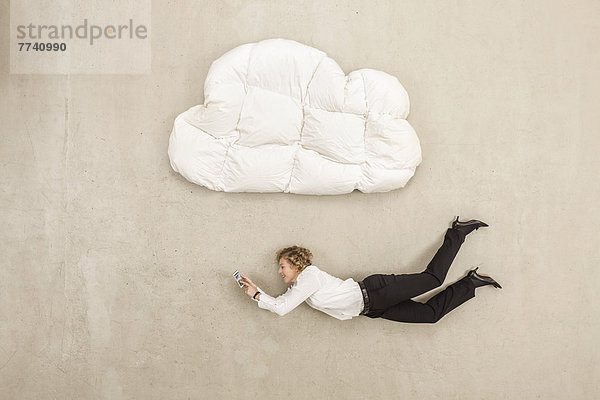 Geschäftsfrau hält Handy und fliegt unter Wolkenform Kissen