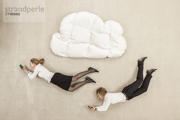 Geschäftsfrauen halten Handy und fliegen unter Wolkenform Kissen