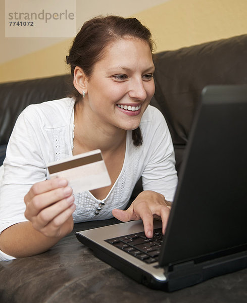 Junge Frau online einkaufen von zu Hause aus mit Laptop und Kreditkarte
