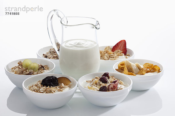 Joghurtkaraffe um Schalen aus Müslijoghurt mit Früchten auf weißem Hintergrund