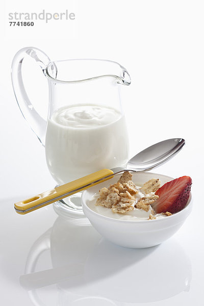 Schale Müslijoghurt mit Erdbeeren neben Joghurtkaraffe auf weißem Grund  Nahaufnahme