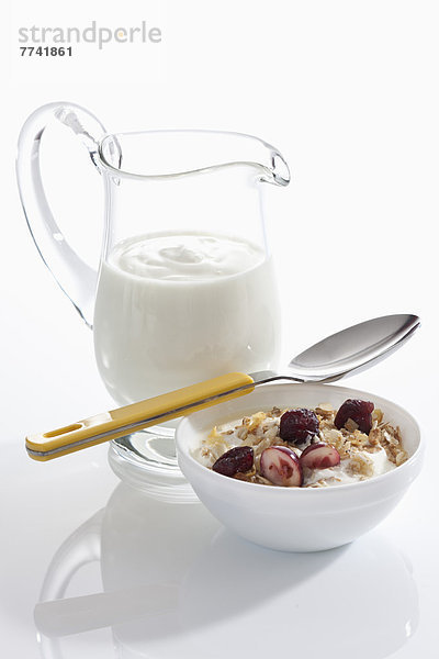Schale Müslijoghurt mit Preiselbeeren neben Joghurtkaraffe auf weißem Grund  Nahaufnahme