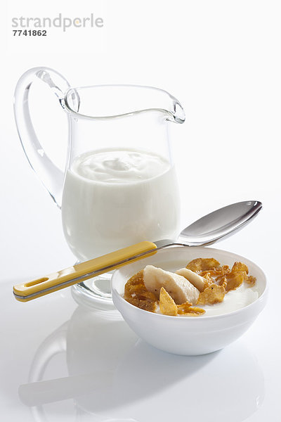 Schale Müslijoghurt mit Banane neben Joghurtkaraffe auf weißem Grund  Nahaufnahme