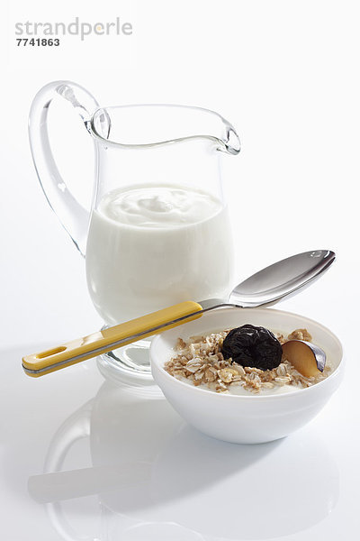 Schale Müslijoghurt mit Pflaume neben Joghurtkaraffe auf weißem Grund  Nahaufnahme