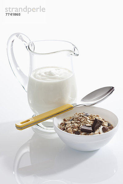 Schale Müslijoghurt mit Schokolade neben Joghurtkaraffe auf weißem Hintergrund  Nahaufnahme