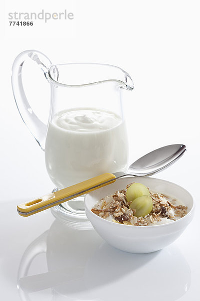 Schale Müslijoghurt mit Trauben neben Joghurtkaraffe auf weißem Grund  Nahaufnahme