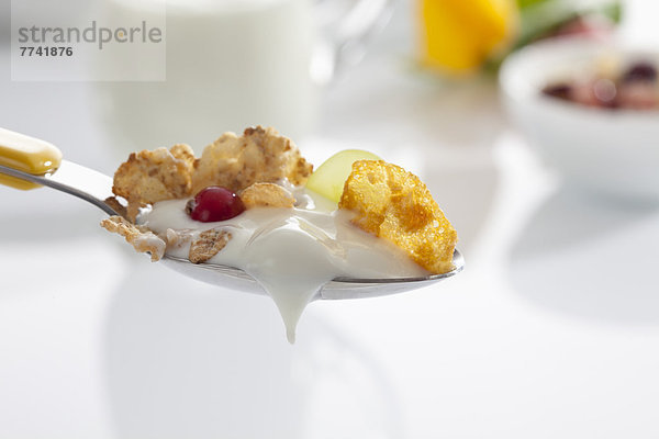 Löffel Joghurt mit Cornflakes und Früchten auf weißem Grund  Nahaufnahme