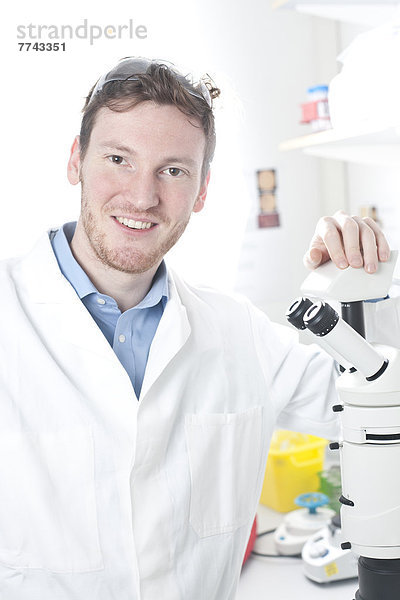Deutschland  Porträt eines jungen Wissenschaftlers mit Mikroskop im Labor  lächelnd
