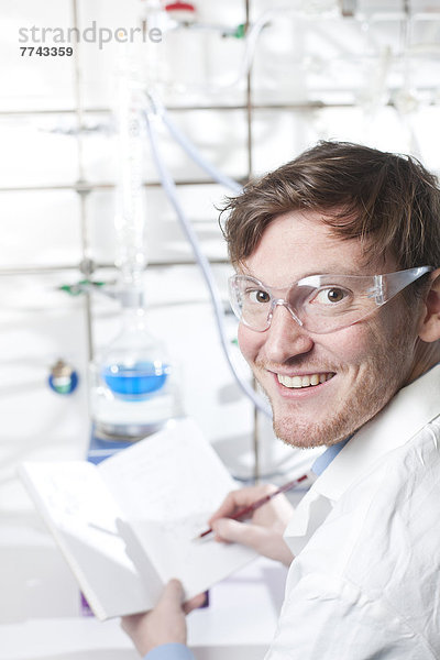 Deutschland  Porträt eines jungen Wissenschaftlers  der sich Notizen macht  lächelnd
