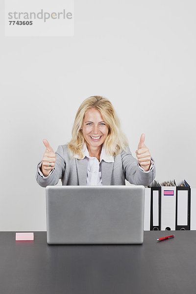 Portrait der Geschäftsfrau mit Laptop und Daumen hoch  lächelnd