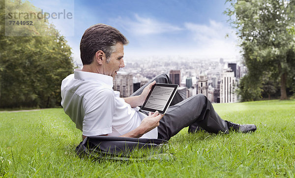 USA  New York  Mann auf Gras sitzend und mit digitalem Tablett  Stadt im Hintergrund