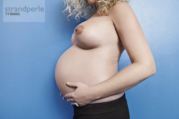 Schwangere Frau mit Bauch und Brüsten vor blauem Hintergrund