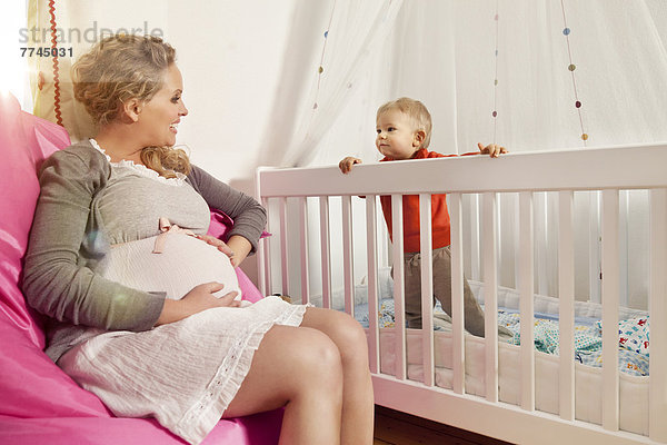 Deutschland  Bonn  Schwangere Mutter sitzend auf Bohnensack mit Sohn im Kinderbett  lächelnd