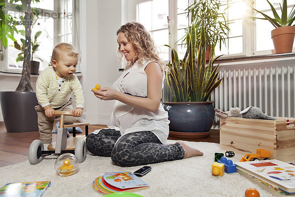 Deutschland  Bonn  Schwangere Mutter spielt mit Sohn im Wohnzimmer  lächelnd