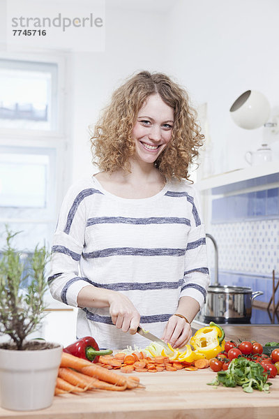 Junge Frau beim Gemüsehacken in der Küche  lächelnd  Portrait