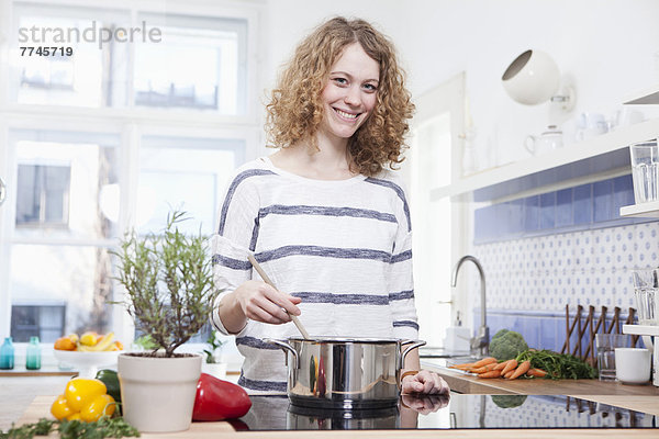 Junge Frau beim Kochen in der Küche  lächelnd  Portrait