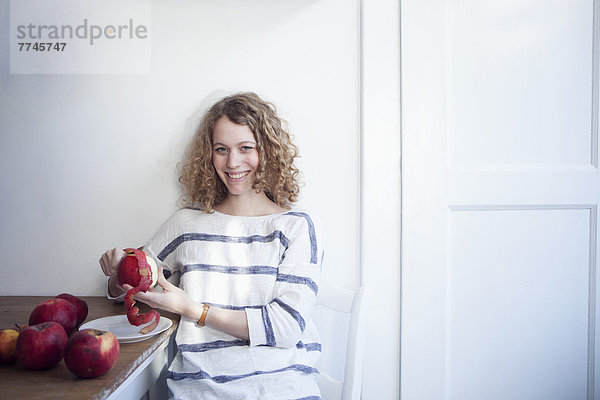 Junge Frau am Tisch sitzend und Äpfel schälend  lächelnd
