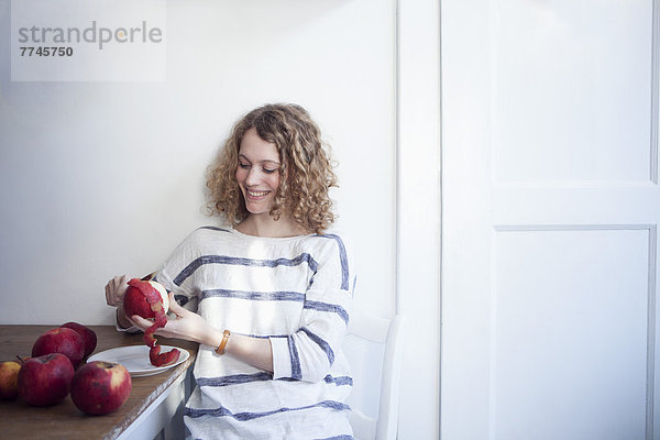 Junge Frau am Tisch sitzend und Äpfel schälend  lächelnd