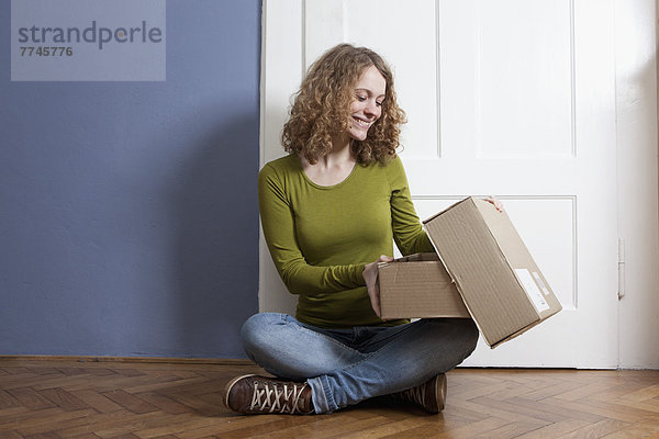 Junge Frau auf dem Boden sitzend und Postpaket öffnend  lächelnd