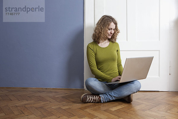 Junge Frau auf dem Boden sitzend und mit Laptop