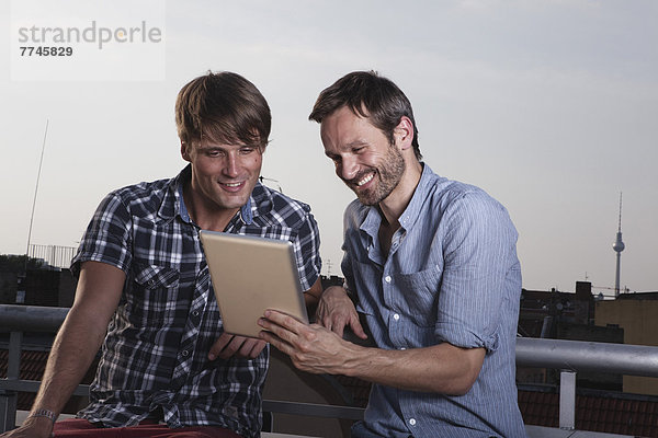 Männer mit digitalem Tablett auf der Dachterrasse  lächelnd