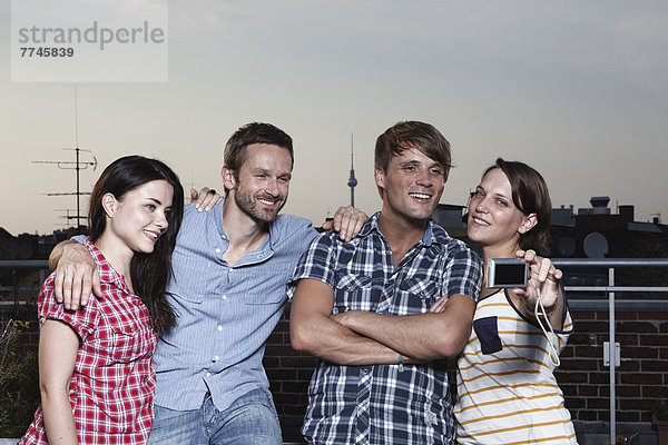 Deutschland  Berlin  Freundeskreis beim Selbstfotografieren auf der Dachterrasse  lachend