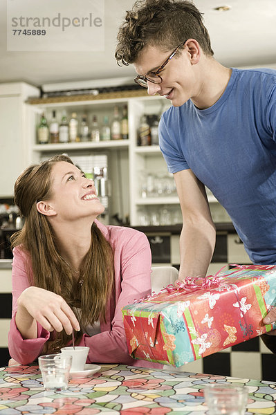 Junger Mann überrascht mit Geschenk an die Frau im Café  lächelnd