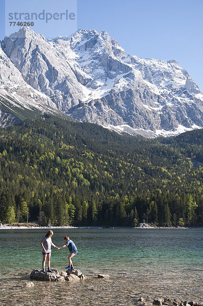 Junge und Mädchen spielen am Eibsee mit Zugspitze im Hintergrund
