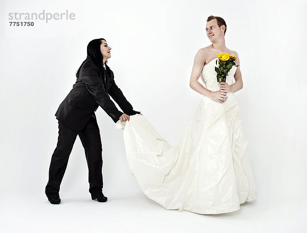 Frau in Anzug hält Bräutigam in Hochzeitskleid die Schleppe  Kleidertausch Hochzeit