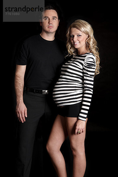 Schwangere Frau und Mann lächeln vor der Kamera