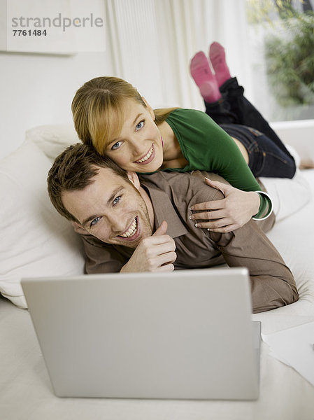 Lächelndes Paar auf der Couch liegend mit Laptop-Computer