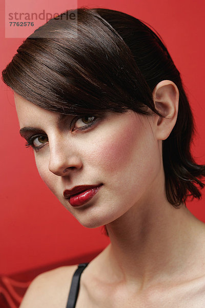 Porträt der geschminkten Frau mit Trageriemen aus schwarzem Oberteil für die Kamera  roter Hintergrund