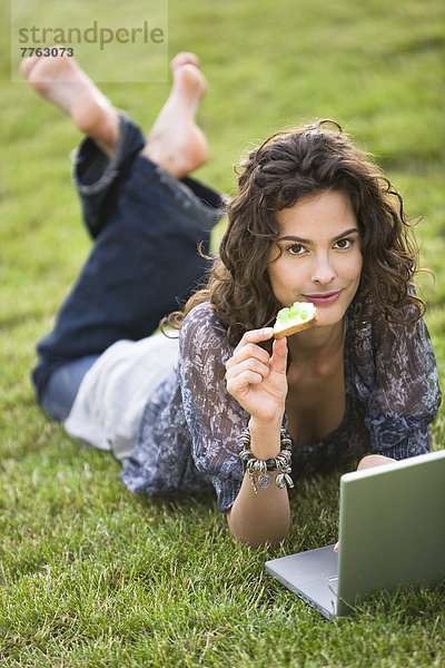 Junge Frau im Gras liegend  mit Laptop-Computer