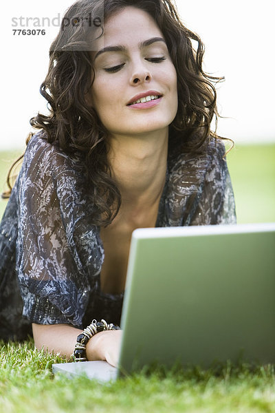 Junge Frau im Gras liegend  mit Laptop-Computer