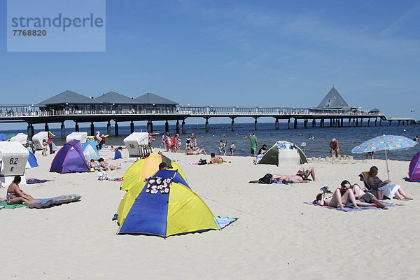 Touristen mit Strandmuscheln am Strand vor der Seebrücke