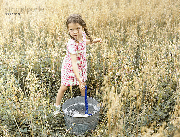 Kleines Mädchen spielt mit einem Eimer Wasser.